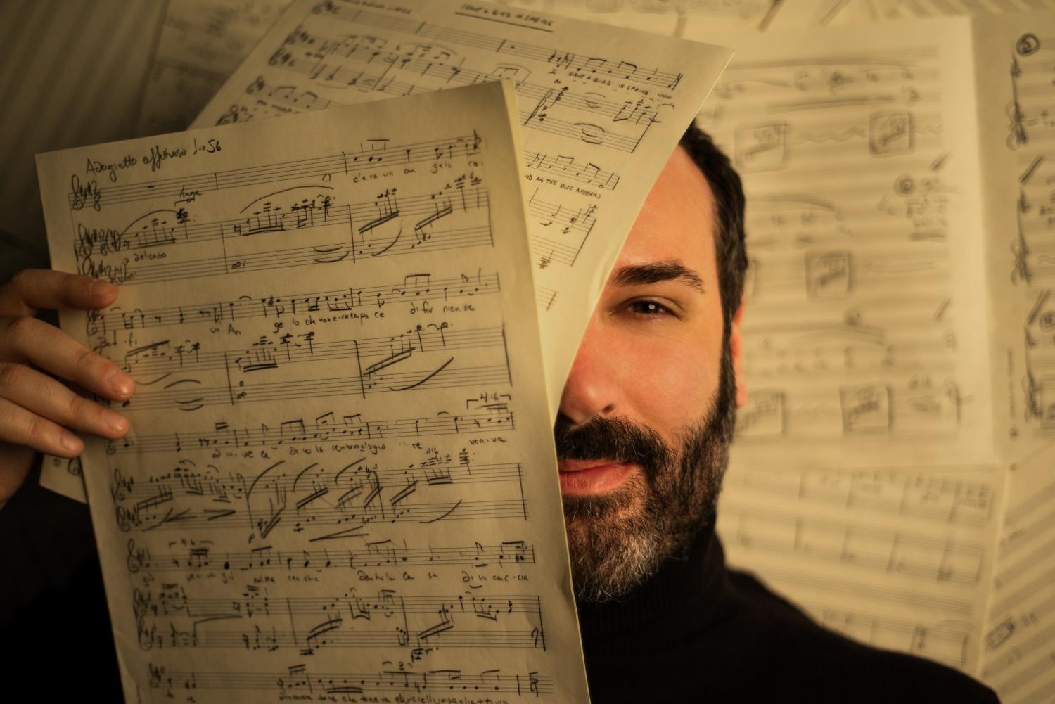composer Raphael Fusco's face partly behind pieces of sheet music