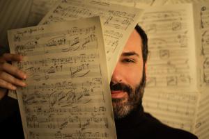 composer Raphael Fusco's face partly behind pieces of sheet music